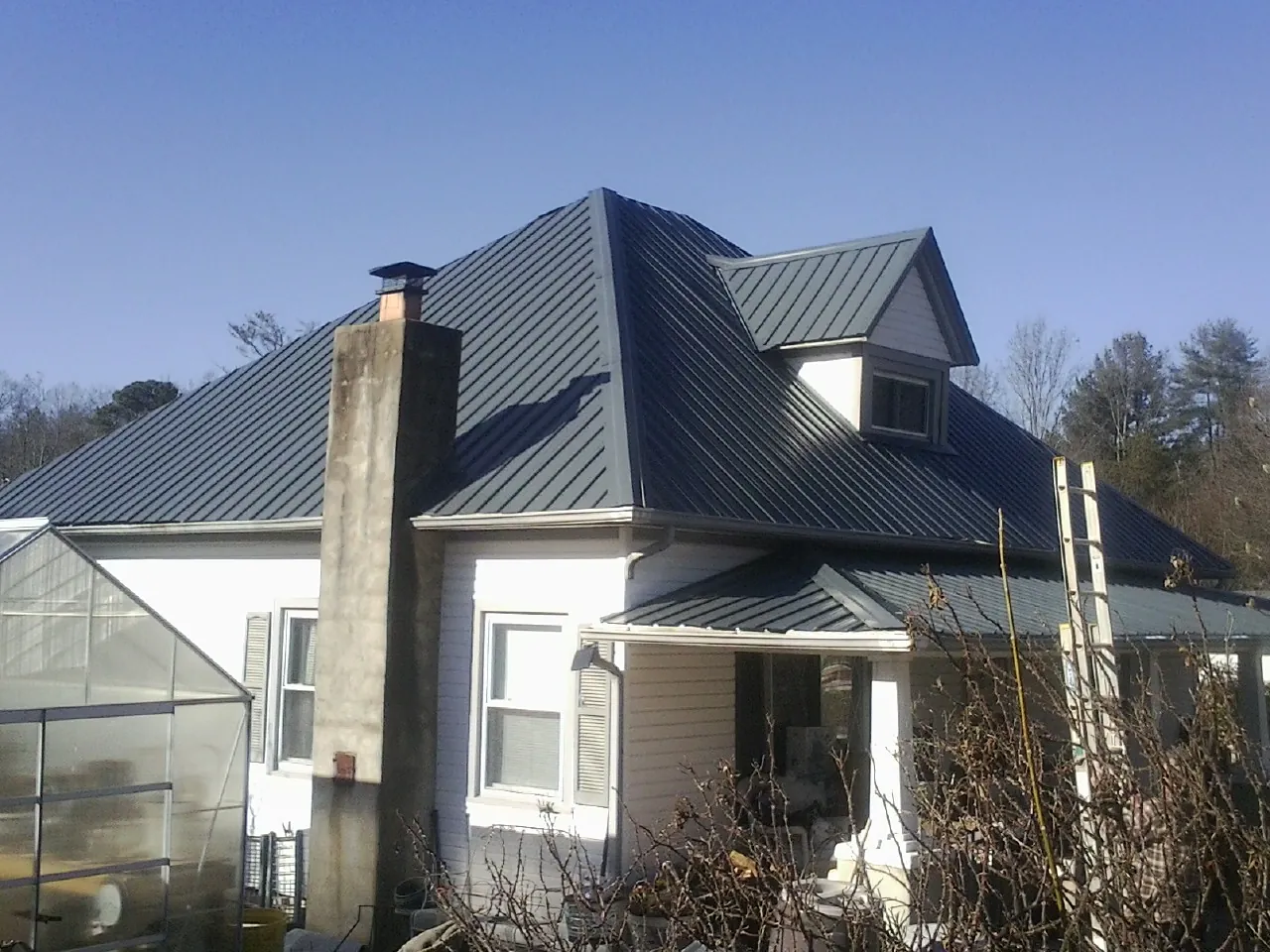 Dark blue standing seam metal roof on a white farmhouse with dormer — Slate & Tile Roof Repair by Roofing Brothers in Orient