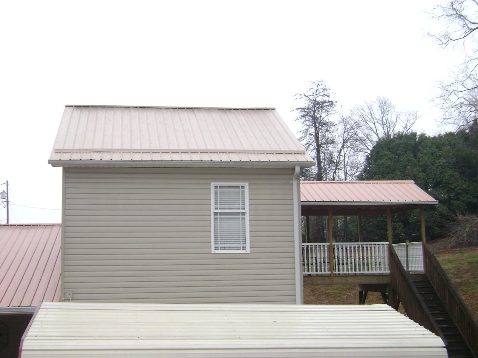 Tan metal roofs on a two story addition and attached porch, from a Roof Replacement job in Orient